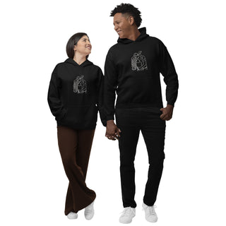 A smiling couple walks hand in hand, each wearing a Maison Memoire black hoodie with a matching embroidered design, symbolizing their bond.