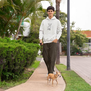 Smiling person wearing a custom embroidered hoodie with a dog portrait, walking a small dog on a sidewalk lined with greenery.