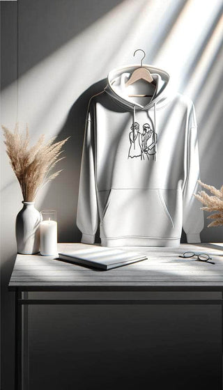 Custom Maison Memoire hoodie with an embroidered couple design, elegantly displayed on a wooden hanger in a naturally lit room.