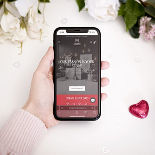 Hand holding a smartphone displaying Maison Memoire's online store with the message "Our Passion is Your Story," emphasizing easy mobile shopping.